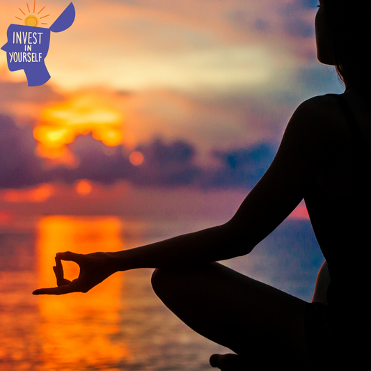 A silhouette of a person meditating by the ocean at sunset, with warm orange and purple hues reflecting on the water.